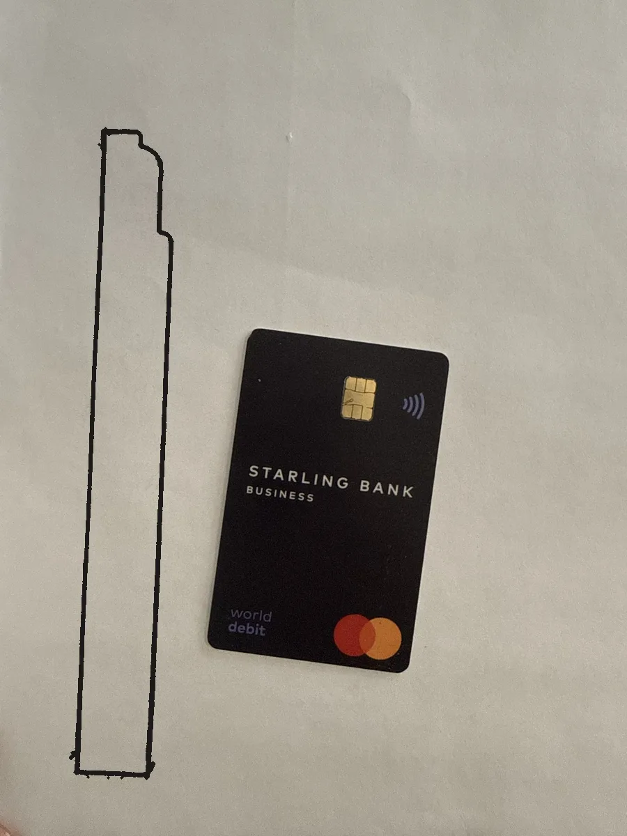 A bold black pen outline of a skirting offcut on white paper, with a bank card lying flat beside it, photographed from directly above